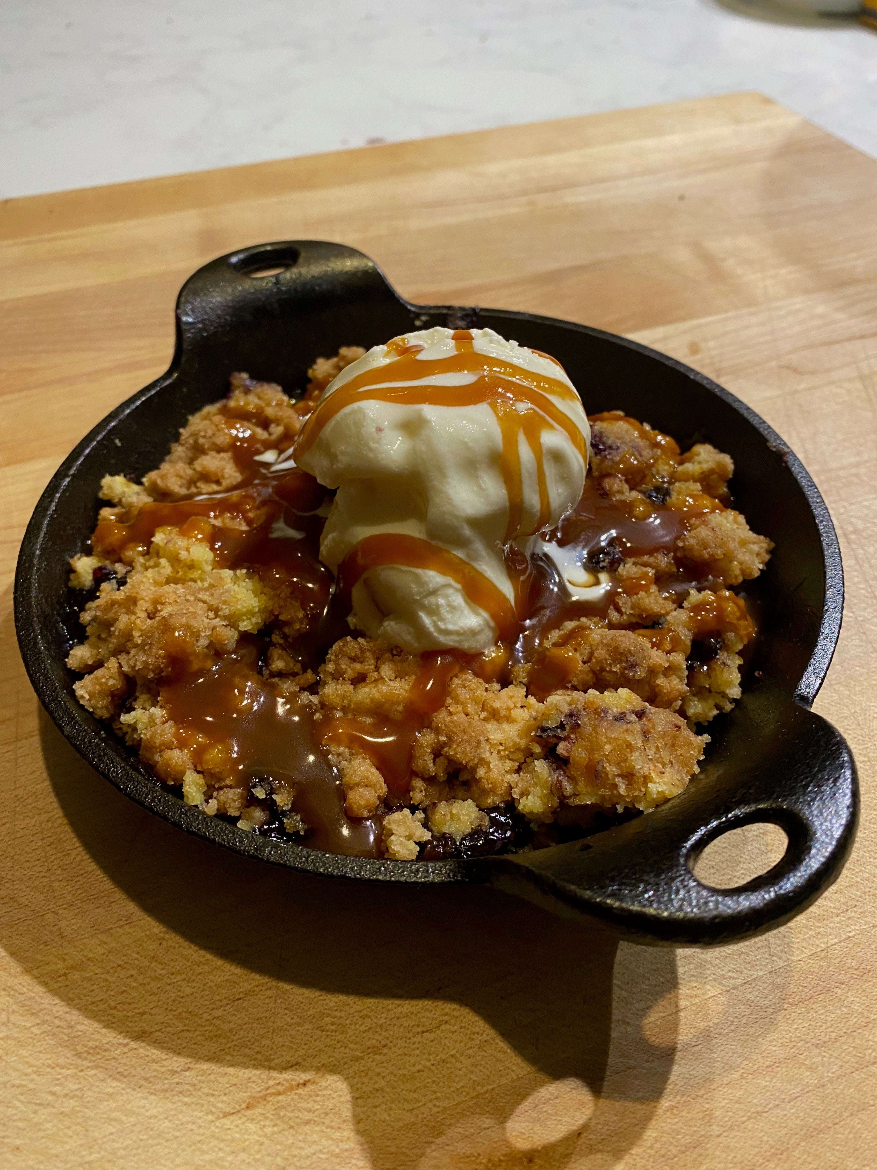 Small cast iron dish with blueberry dump crumble cake with ice cream and caramel