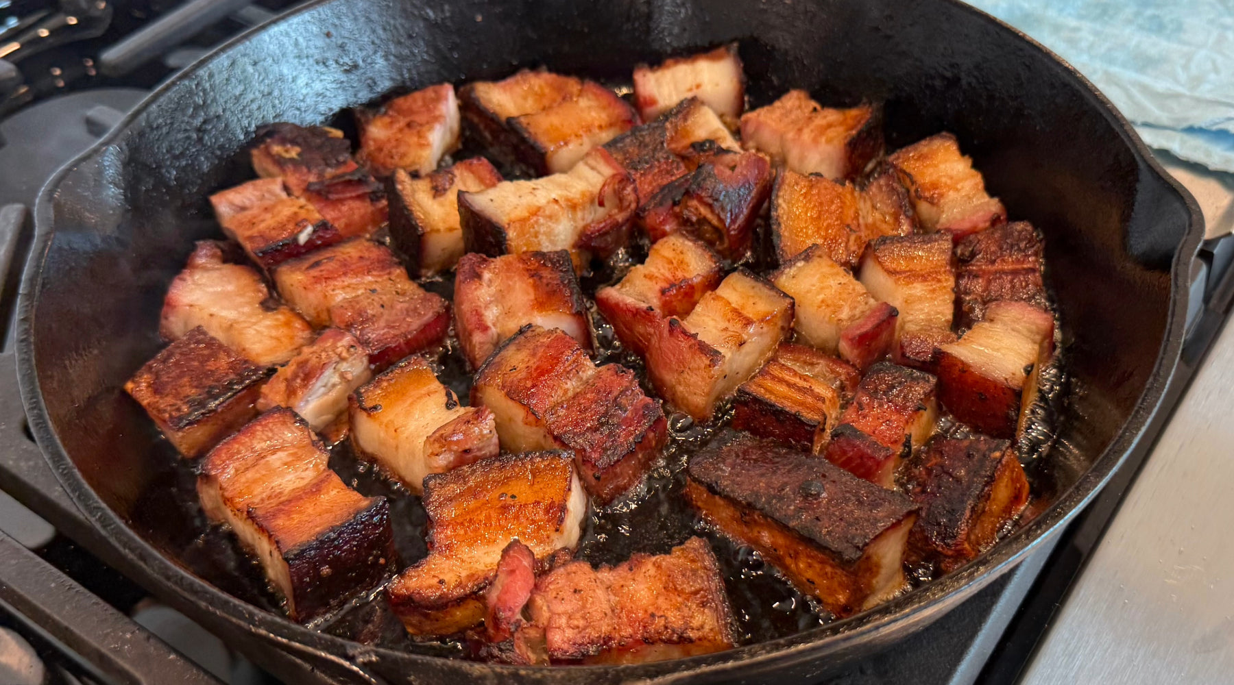 Cubes of pork belly sizzling in a cast iron skillet, seared to a golden brown with crispy edges.