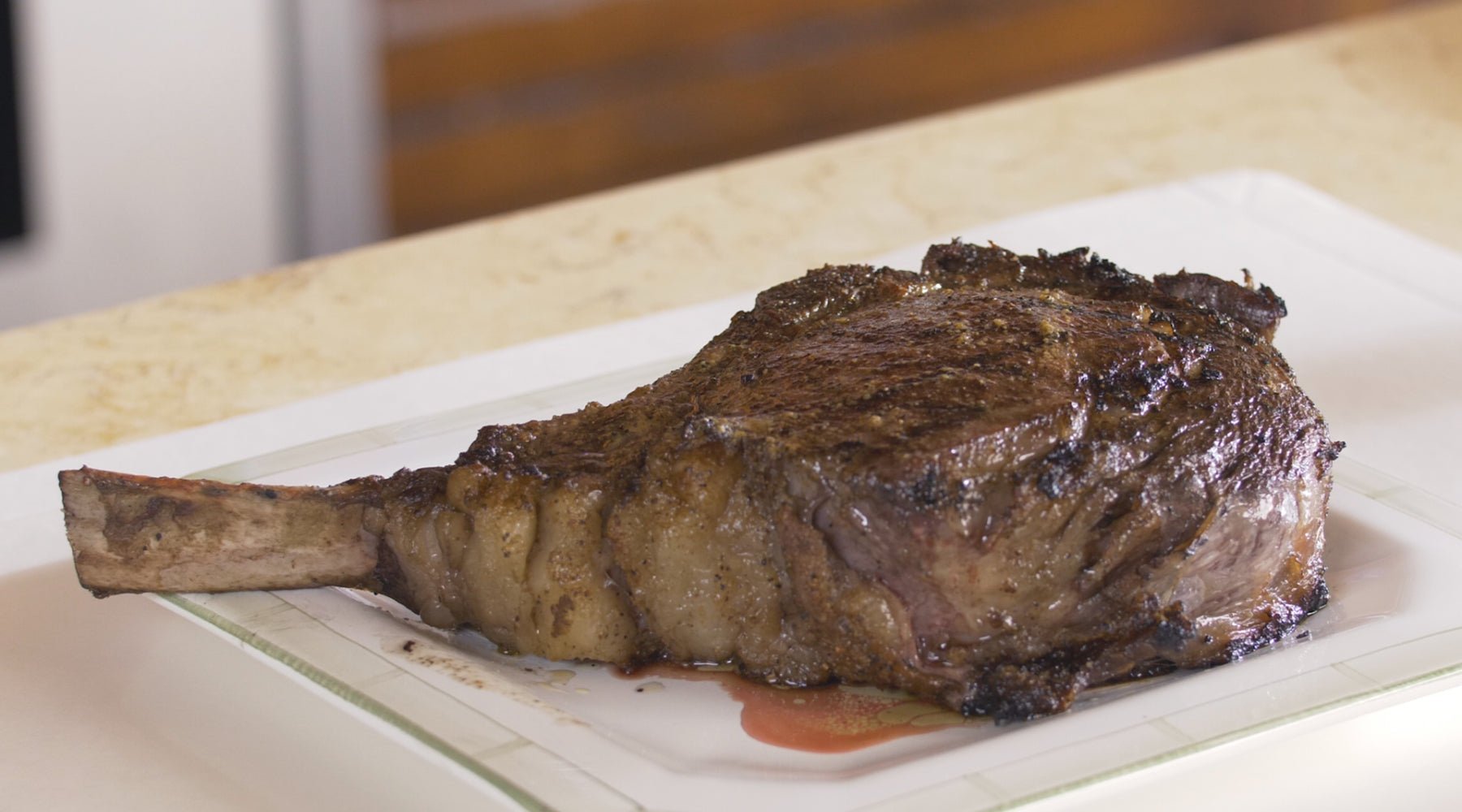 Juicy bone-in ribeye on a white plate that is resting on the counter.
