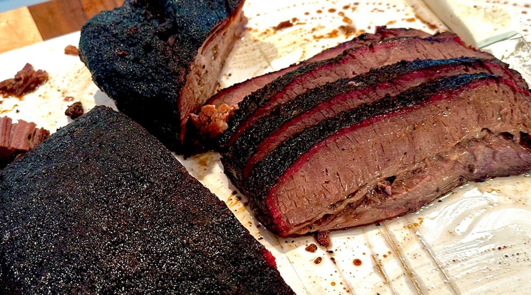 The image shows a close-up view of a smoked beef brisket. The brisket has been sliced into thick pieces, revealing a juicy, tender interior with a noticeable smoke ring beneath a dark, crispy bark.