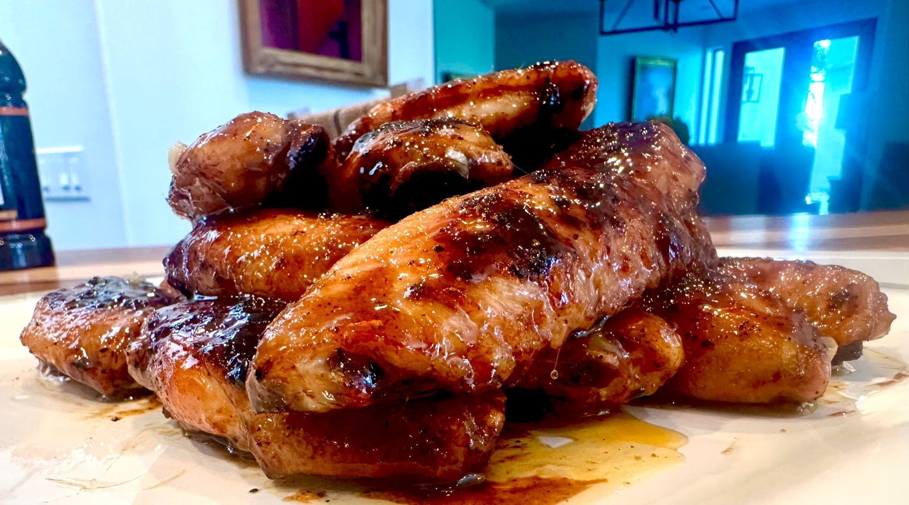 A plate piled high with glazed chicken wings, each coated in a rich, shiny sauce, displayed on a wooden table.