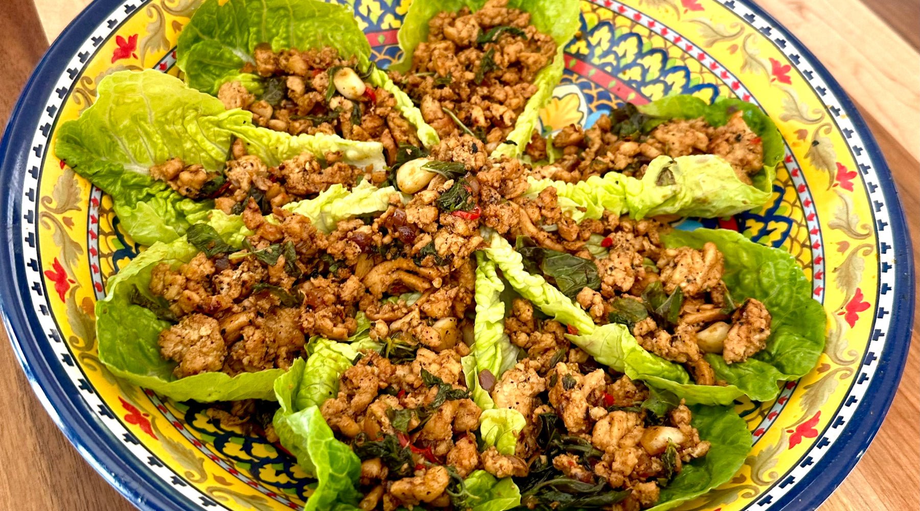 Colorful plate of lettuce wraps filled with seasoned ground meat, herbs, and vegetables arranged in a circular pattern.