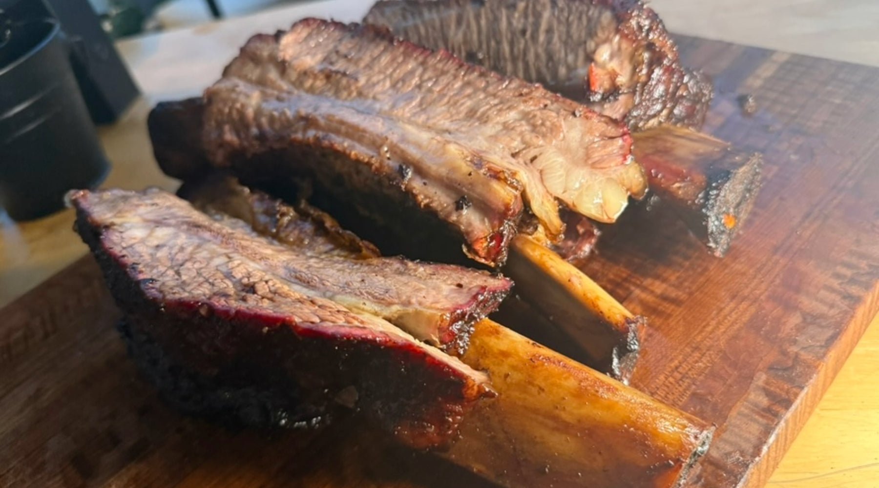 Smoked beef ribs with a dark bark and visible smoke ring, sliced and served on a wooden cutting board.