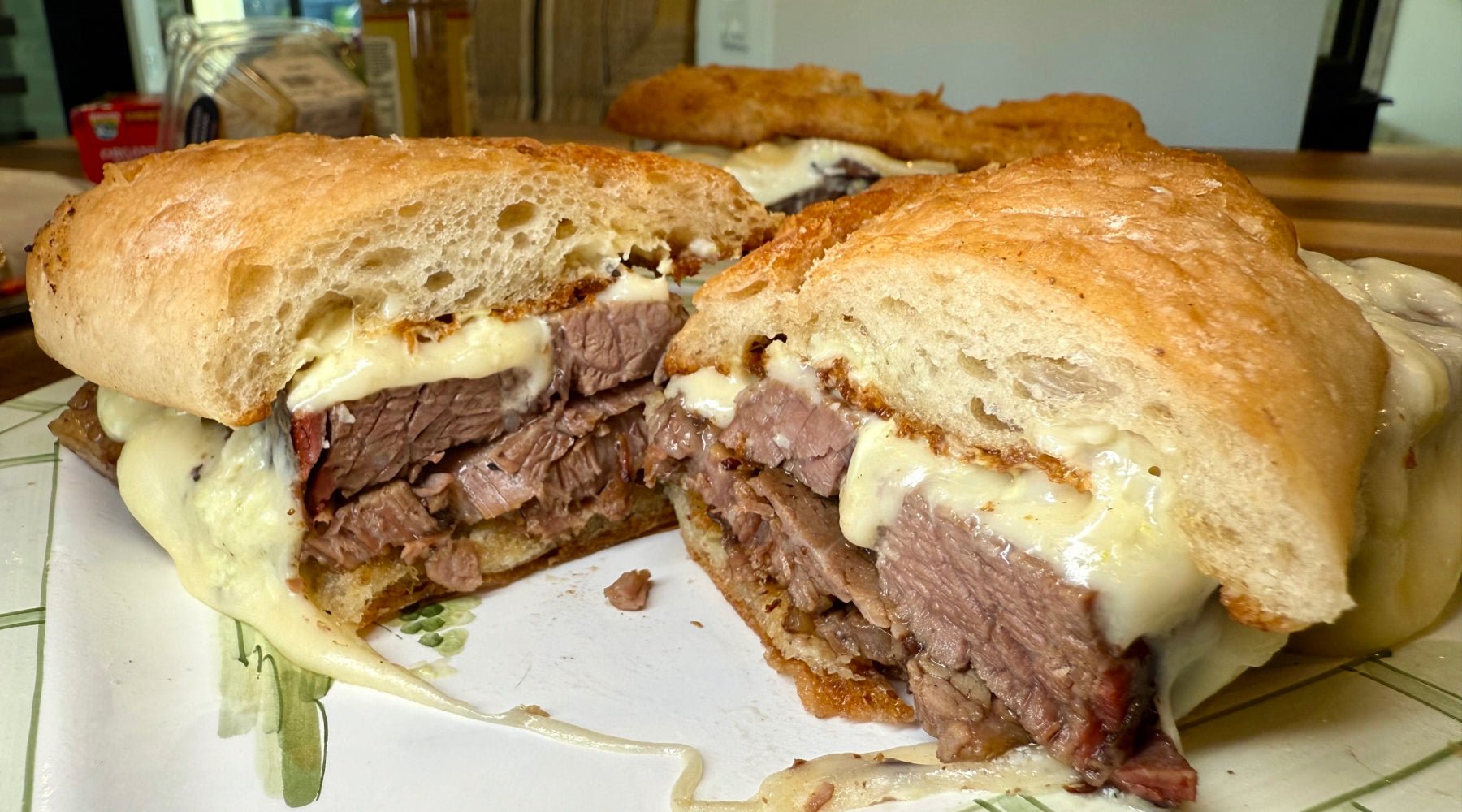 Sliced sandwich filled with thick-cut roast beef and melted cheese on crusty bread, served on a patterned plate.