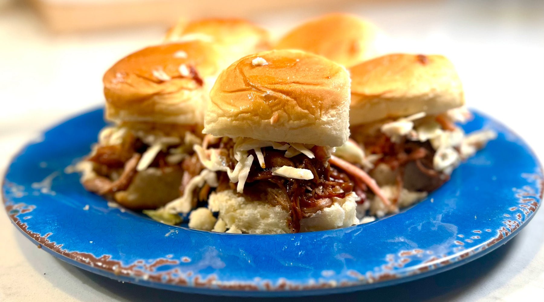Pulled pork sliders with miso macadamia slaw on glossy buns, served on a vibrant blue plate.