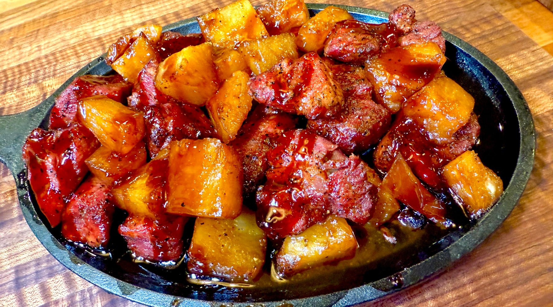 Glazed chunks of roasted pork and pineapple served in a cast iron skillet on a wooden table.