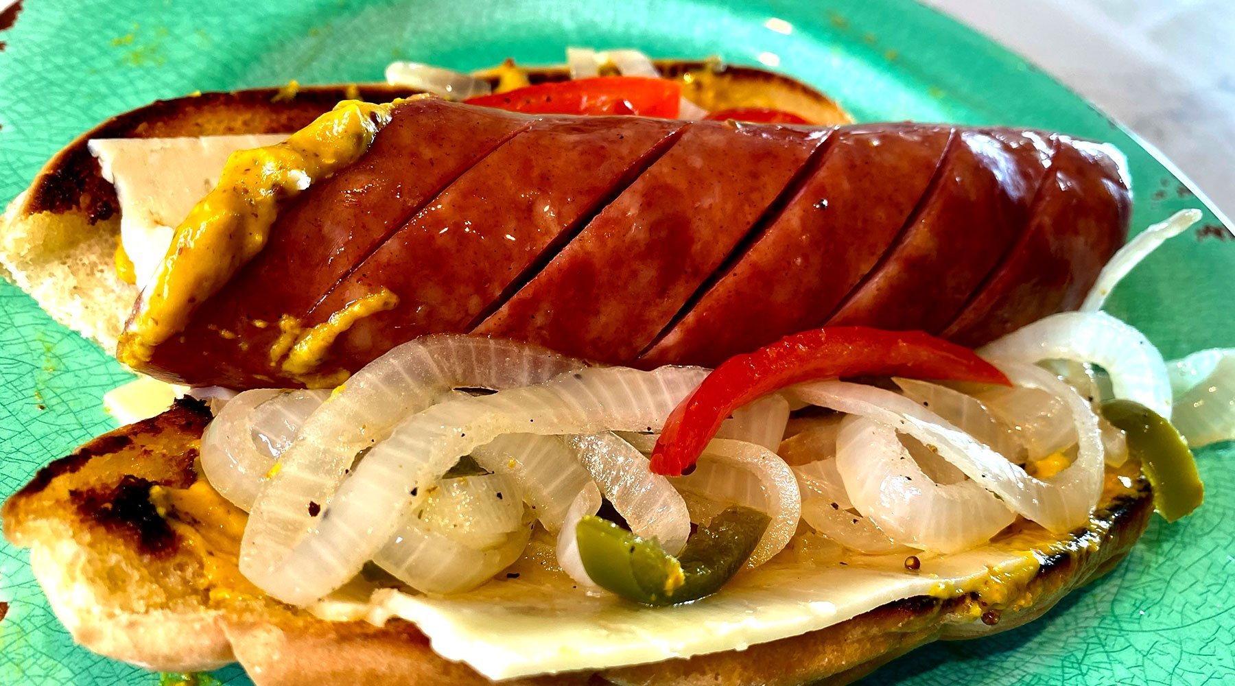 Plate that has a large sausage cut in a spiral that is sitting on top of a bun with onions and peppers