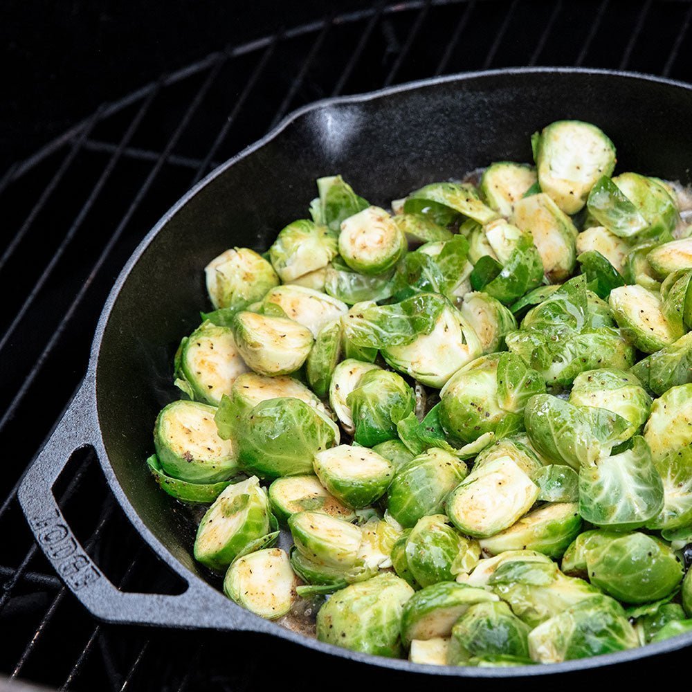 Cast iron pan on the drum smoker that has sliced brussel sprouts that are seasoned with Big Poppa Smokers' Desert Gold.