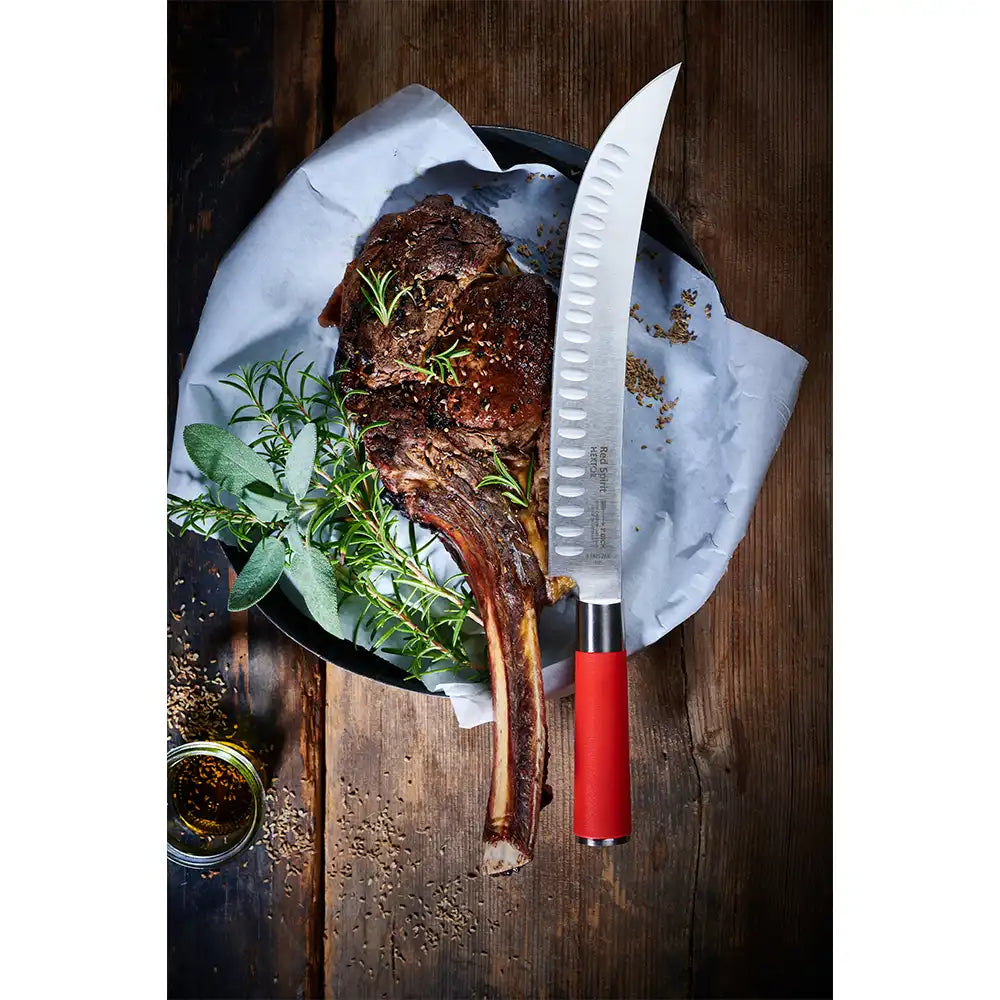 Cooked tomahawk steak on parchment-lined plate with herbs and red-handled slicing knife.