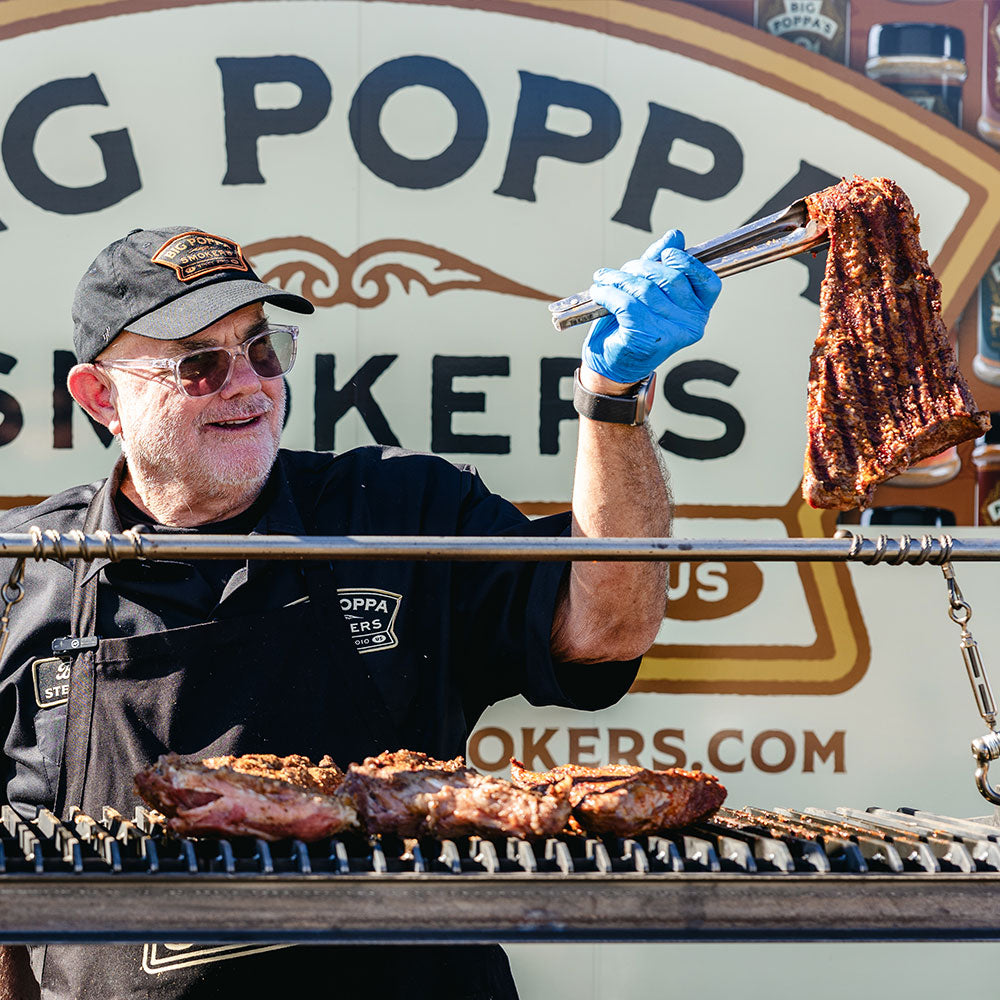 Close up of Sterling "Big Poppa" Ball holding a piece of Double Secret Tri-Tip that has been cooking on the grill.