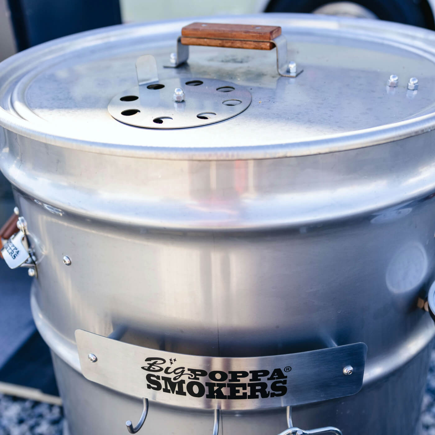 Stainless steel smoker with 'BigPoppa Smokers' branding on a blurred background