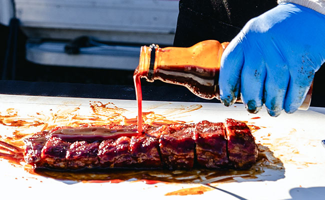 Beauty shot of Big Poppa Smokers Granny's sauce being poured over a rack of pork ribs