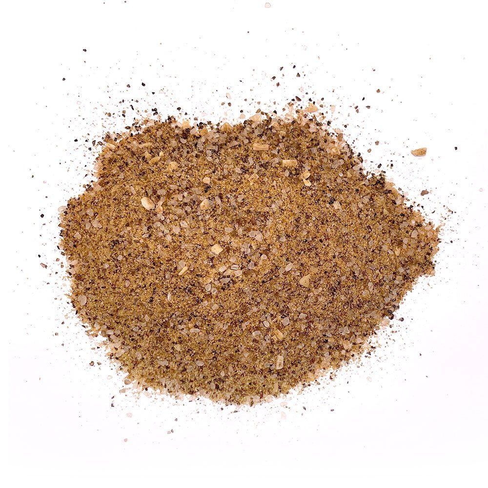 Close-up view of coarse brown seasoning with visible flakes of sea salt, herbs, and spices, ideal for flavoring brisket and steak, spread out on a white background.