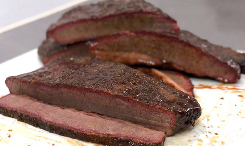 Thick slices of seasoned brisket with a rich bark and pink smoke ring, served on a white plate, demonstrating the juicy and tender texture of the meat.