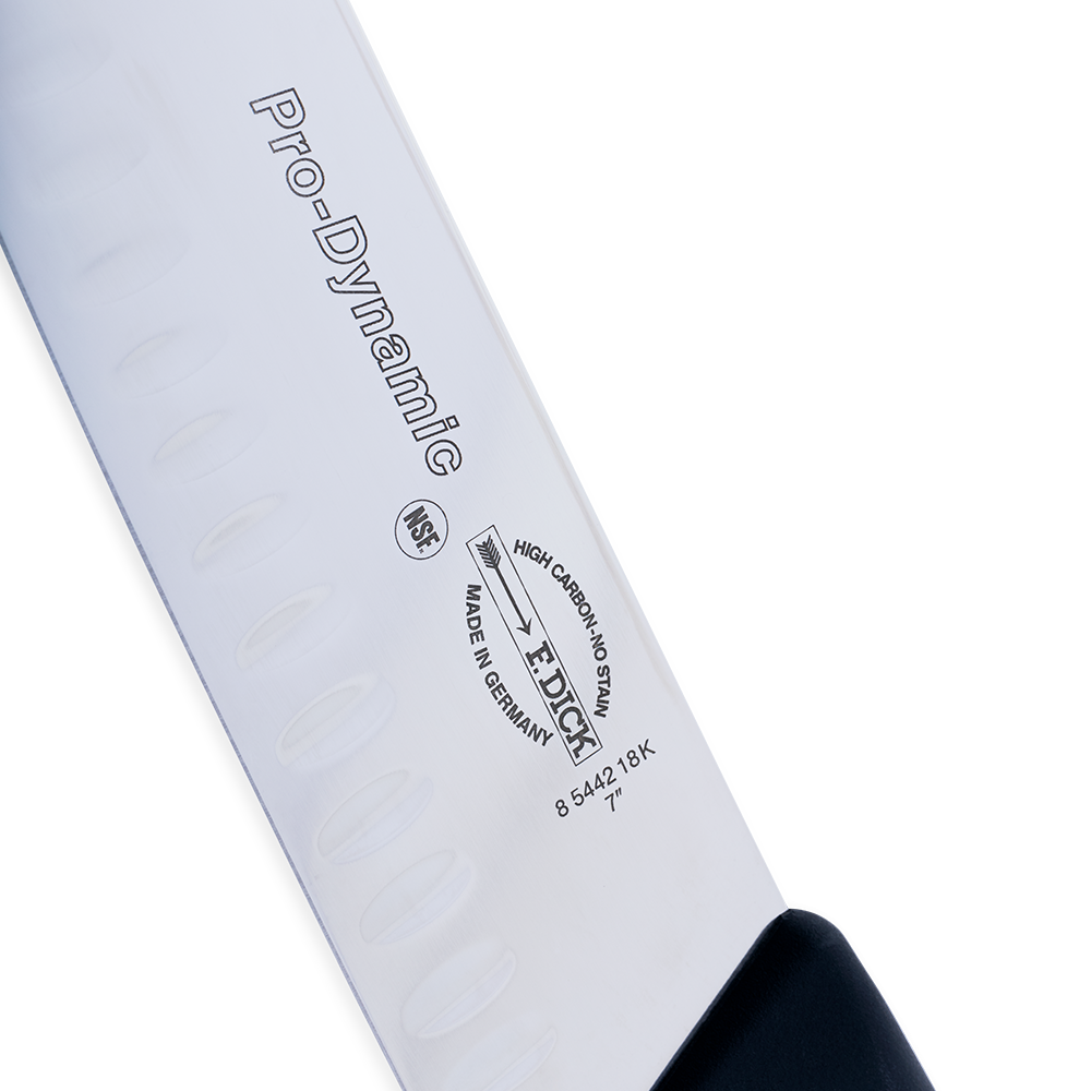 Close-up image of the F. Dick 7" Santoku Kullenschliff - ProDynamic. The knife features a high-carbon stainless steel blade with a kullenschliff edge to prevent food from sticking. It has a black ergonomic handle designed for comfort and control. Displayed on a plain white background, highlighting its sharpness and professional design.