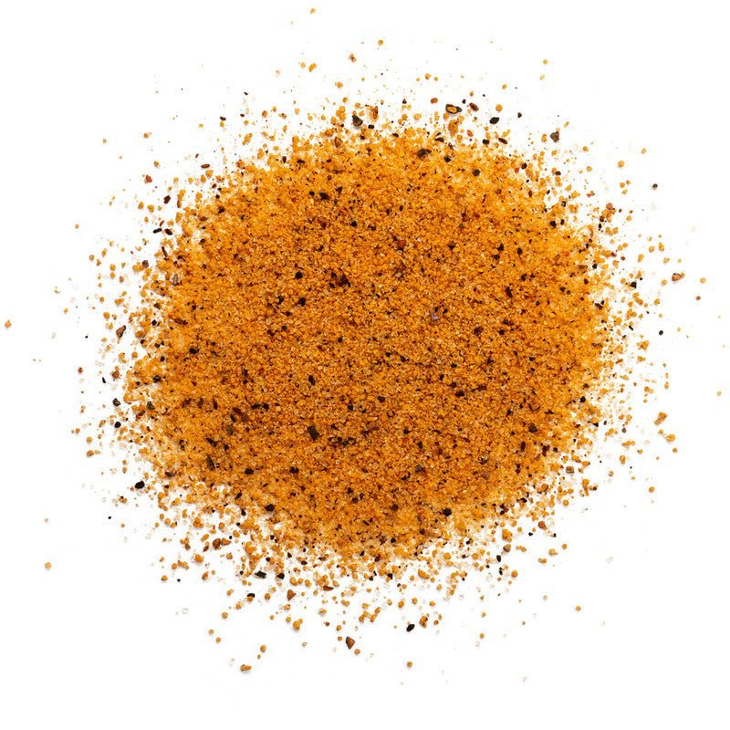 A close-up view of a pile of Meat Church Deez Nuts Pecan Rub. The spice mix is a coarse, reddish-brown powder with visible black pepper flakes.