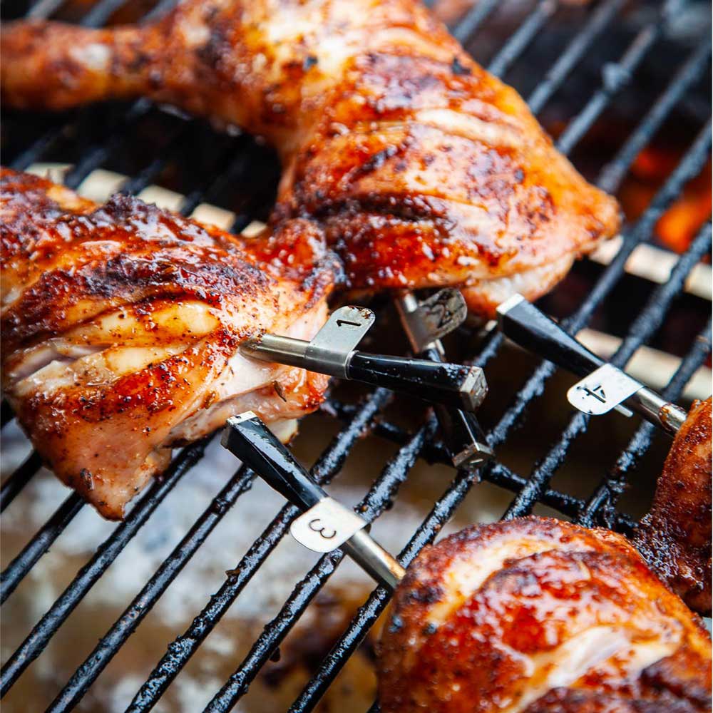 Chicken on the grill that has probes in the chicken thighs. In addition, the probes are labeled to make it easier to monitor.