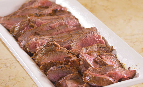 Slices of medium rare grilled steak arranged neatly on a white rectangular serving platter, showcasing a juicy, pink interior.