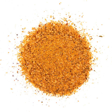 Close-up of a pile of golden-brown barbecue seasoning mix, with visible grains of salt, herbs, and spices, isolated on a white background.