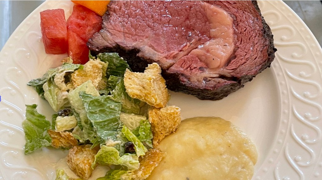 Holiday plate that has prime rib, caesar salad and fruit.