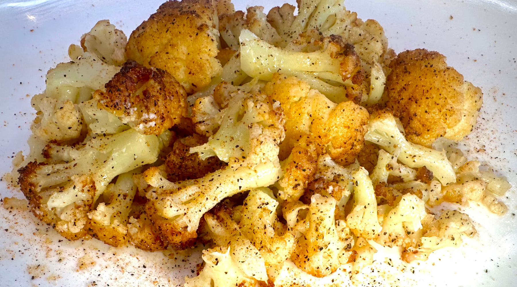 Roasted cauliflower florets seasoned with black pepper and spices, golden and slightly crispy, served on a white plate.