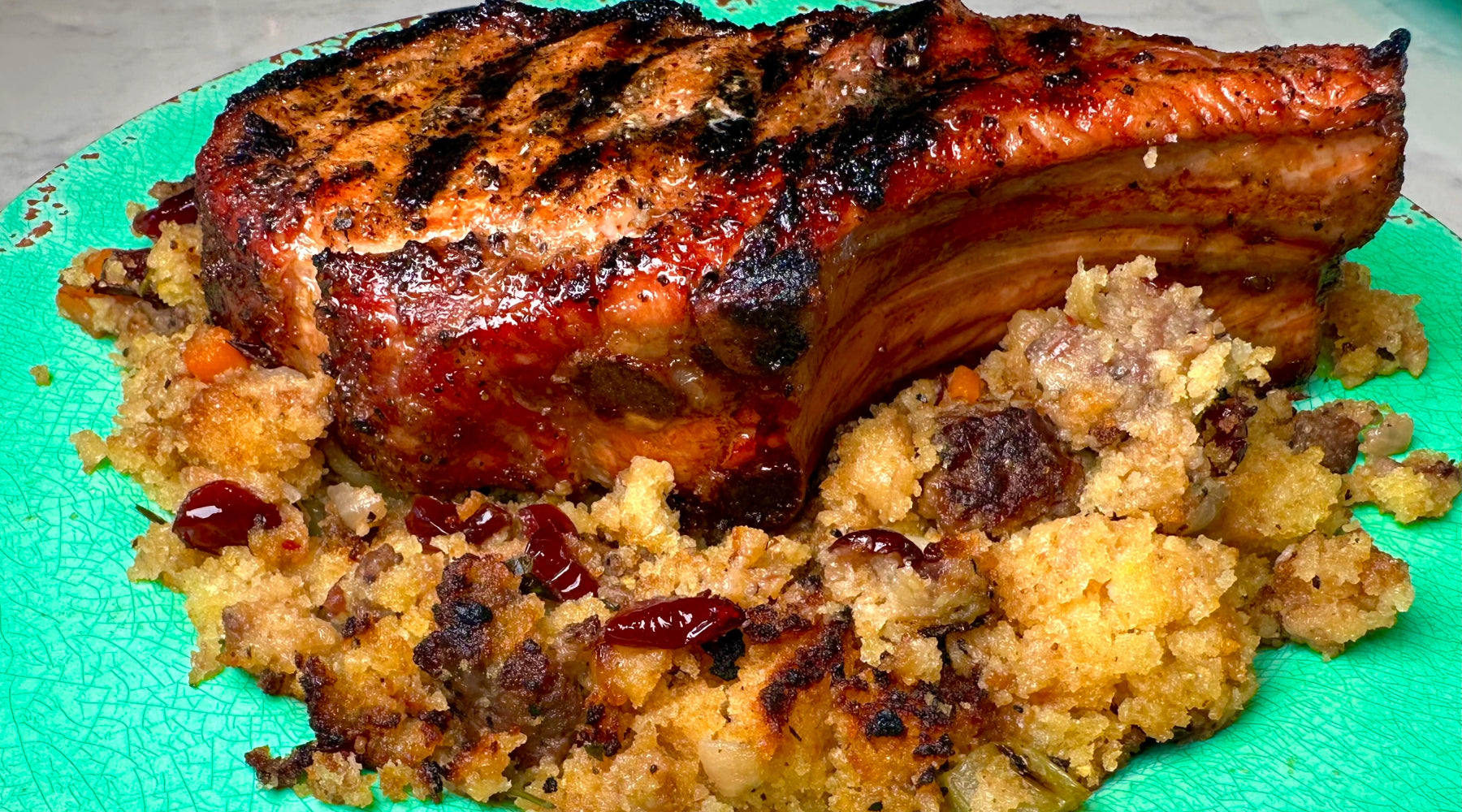 Thick grilled pork chop with a caramelized crust, served over sausage cornbread stuffing on a green plate.