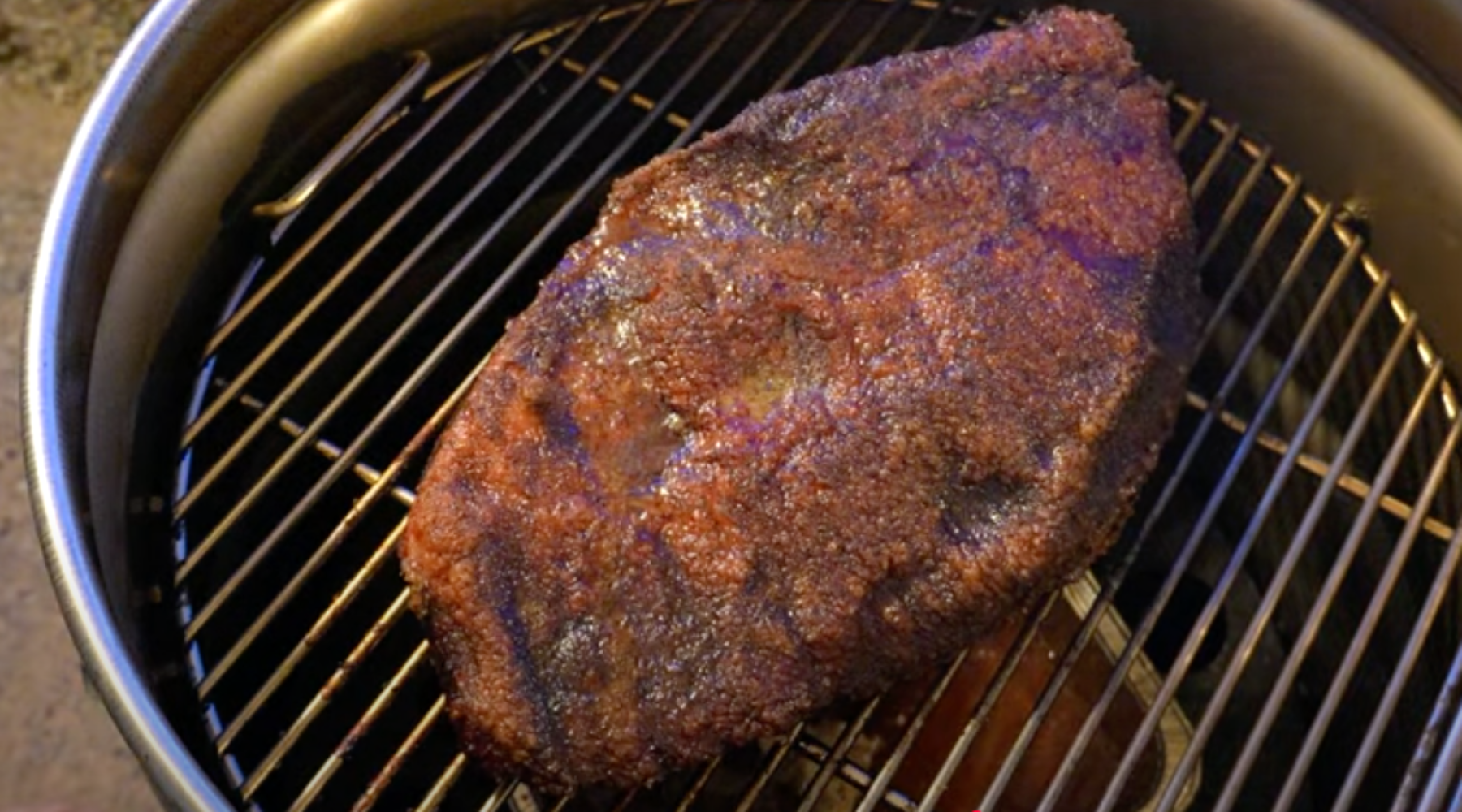 A whole smoked beef brisket with a dark, crispy bark resting on a grill grate.