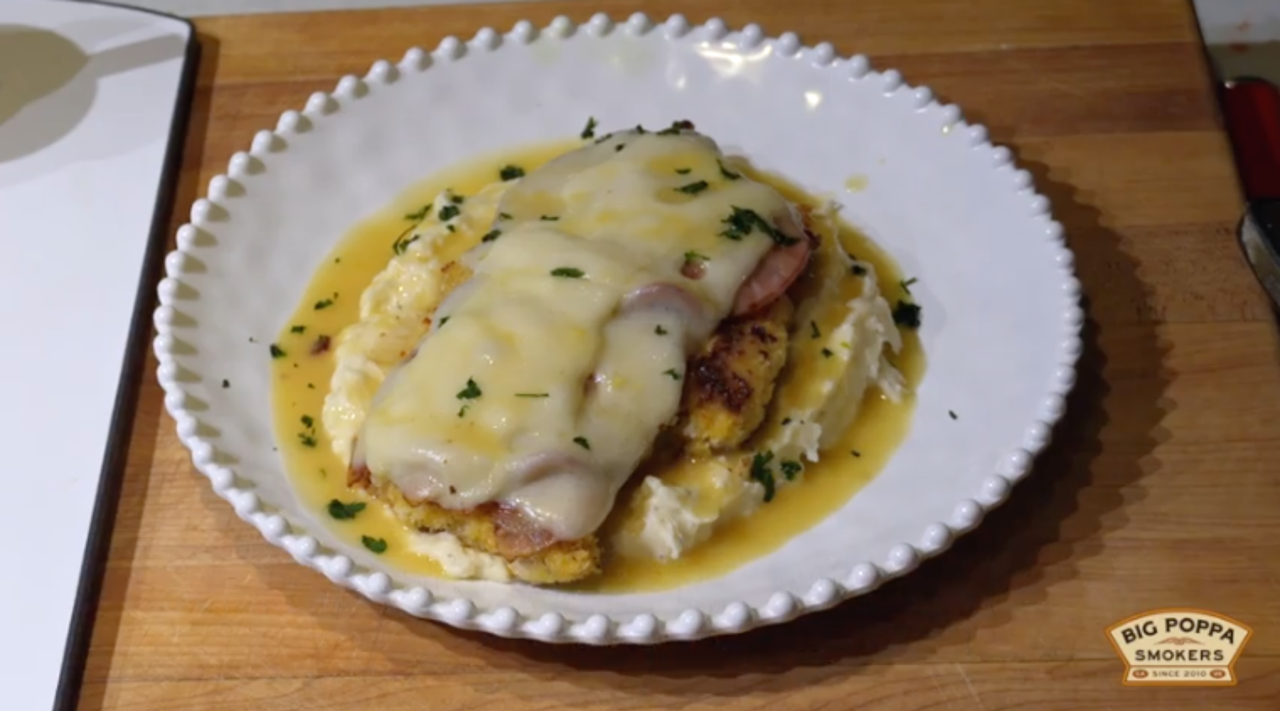 Chicken Cordon Bleu with ham, melted cheese, and gravy over mashed potatoes, garnished with parsley, served on a white plate.