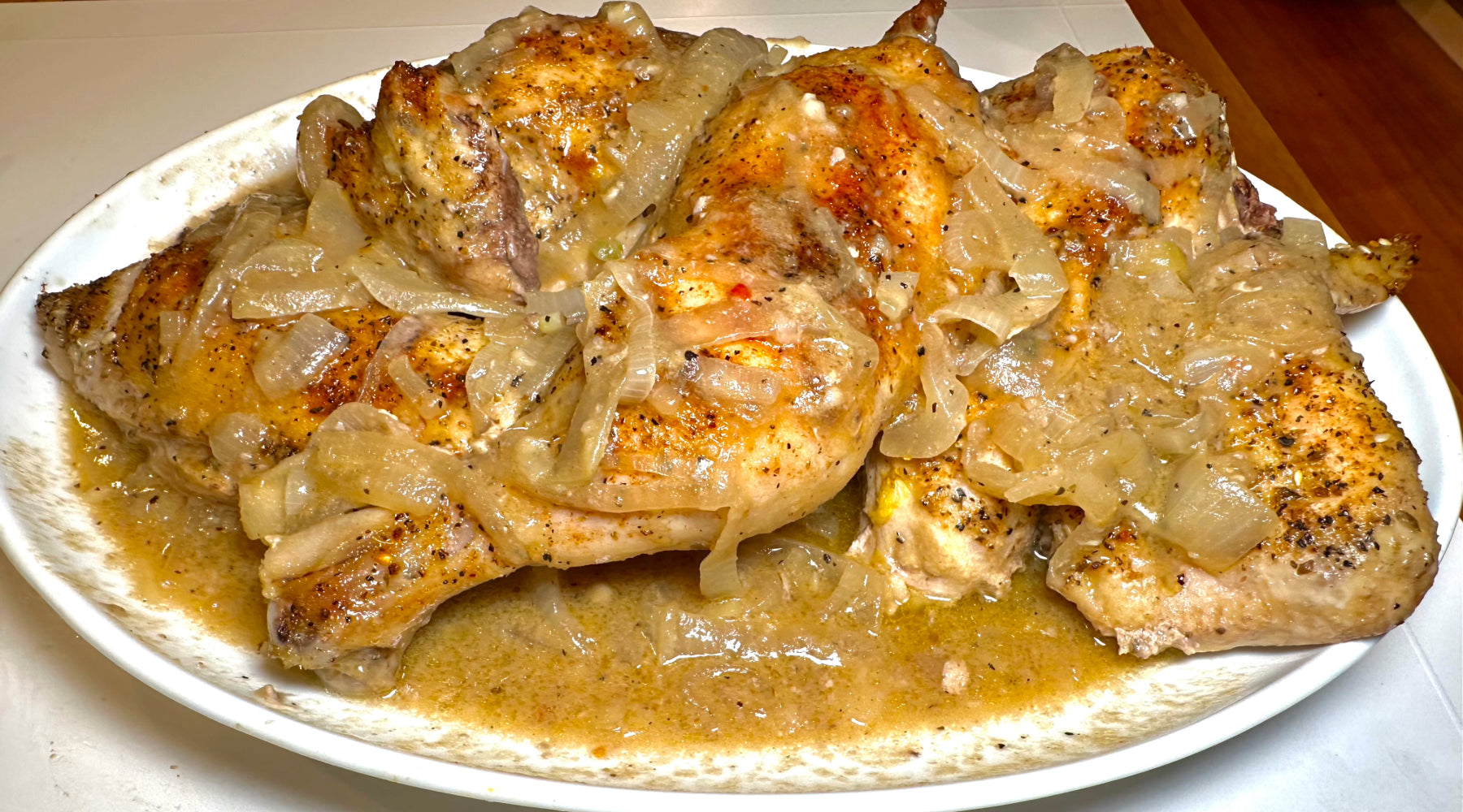 Roasted chicken with onions and gravy on a white plate.