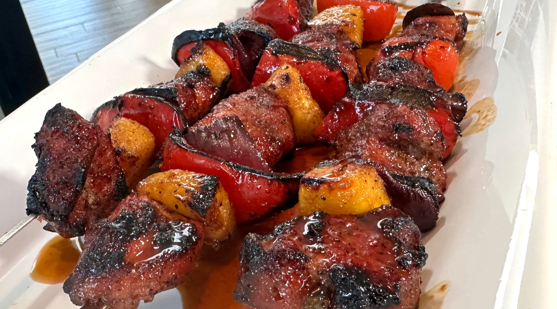 Glazed grilled meat skewers with red bell peppers and pineapple, served on a white platter.