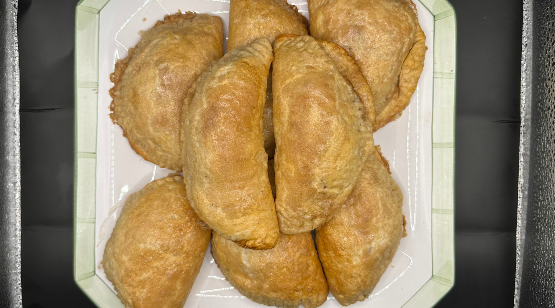 A pile of flaky, baked apple turnovers with crimped edges on a decorative serving platter.