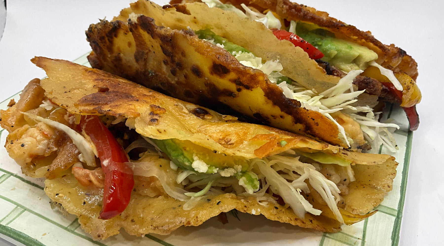 Three crispy tacos filled with shredded cabbage, avocado slices, red bell peppers, and shrimp.
