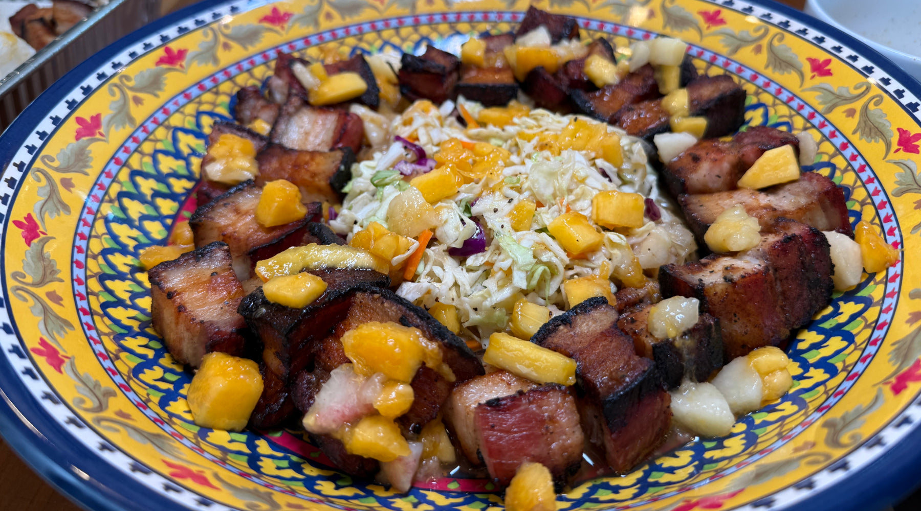Colorful bowl of peach coleslaw topped with grilled pork bites, seasoned with Cuckoo Racha and Little Louie’s Garlic Pepper.