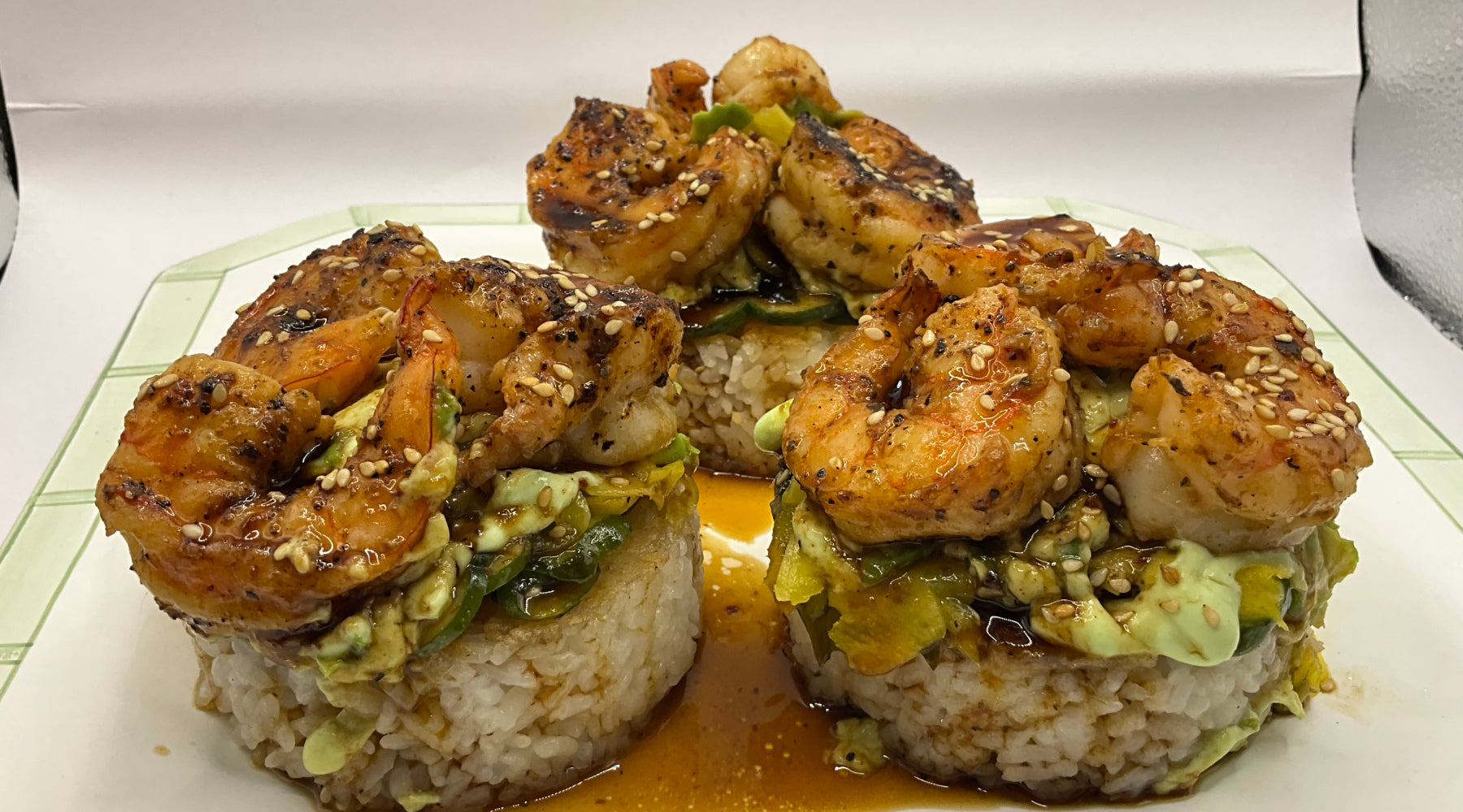 Shrimp and avocado towers on crispy rice, drizzled with wasabi crema and sauce, garnished with sesame seeds.