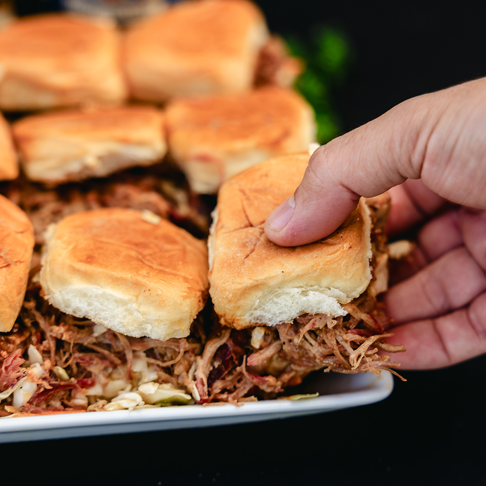 A hand reaching for a pulled pork slider on an King's Hawaiian roll.