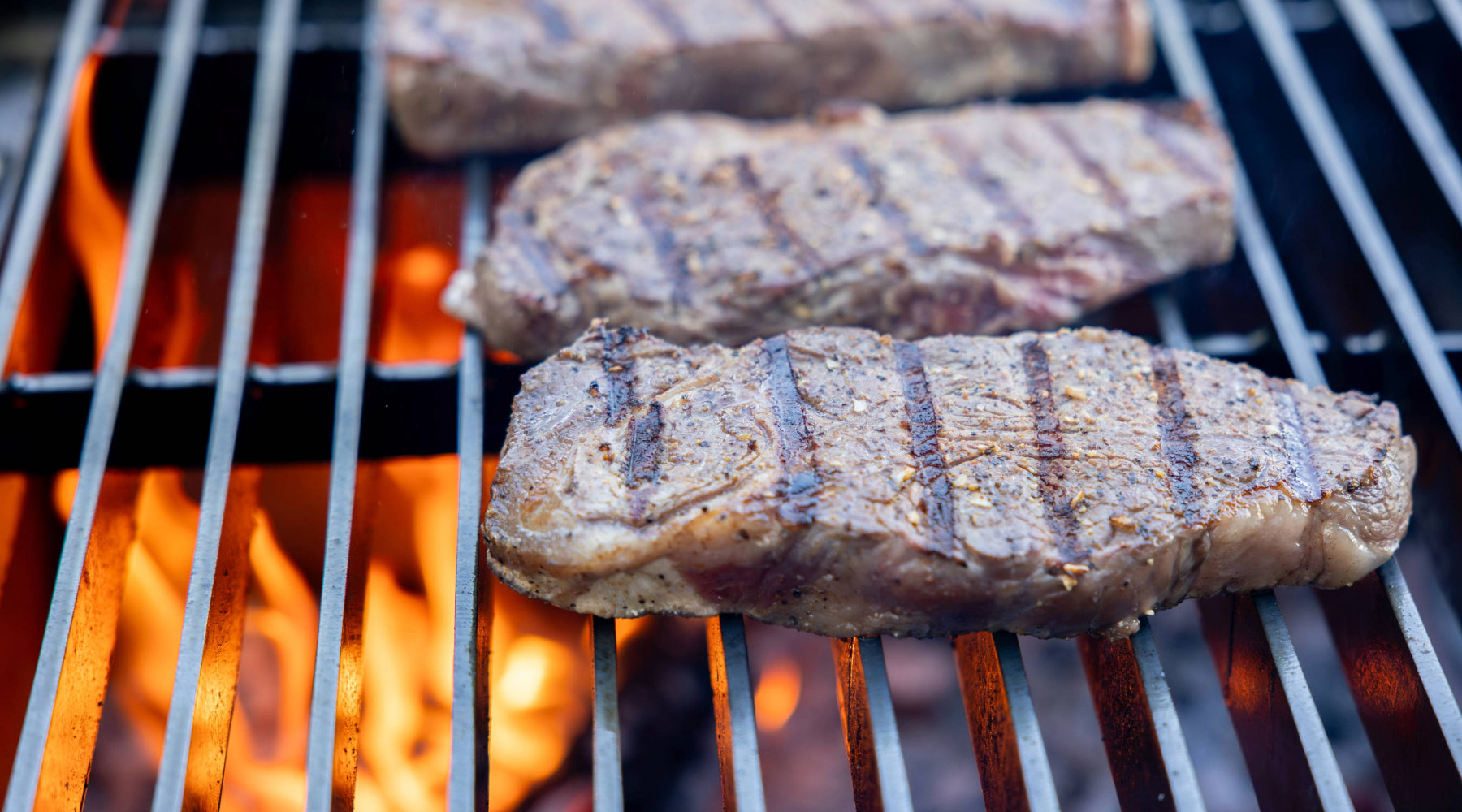 A sizzling steak on a hot grill, featuring distinct char marks and gentle wisps of smoke rising.