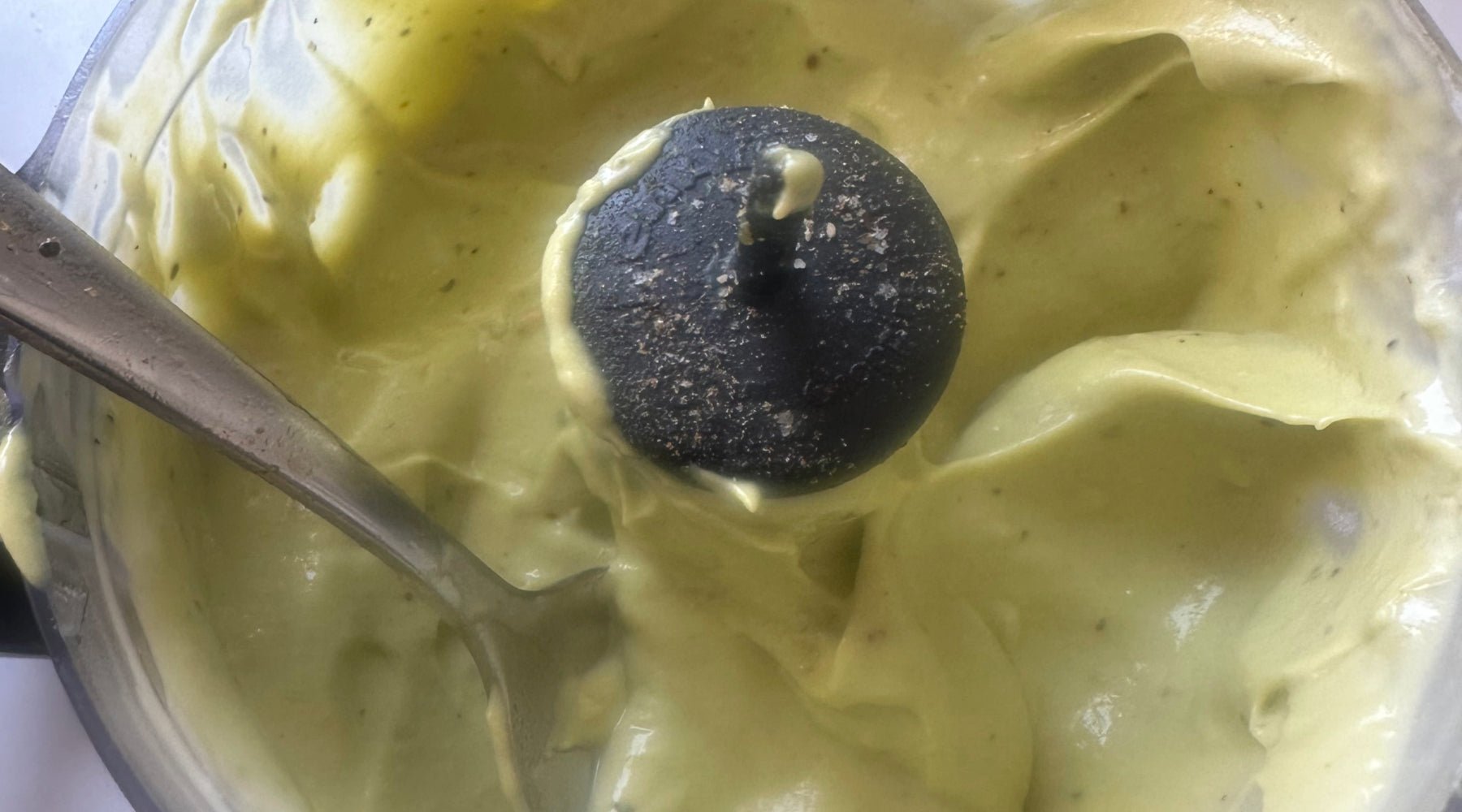 Blender filled with smooth, light green mixture, with a metal spoon and the blender blade visible.