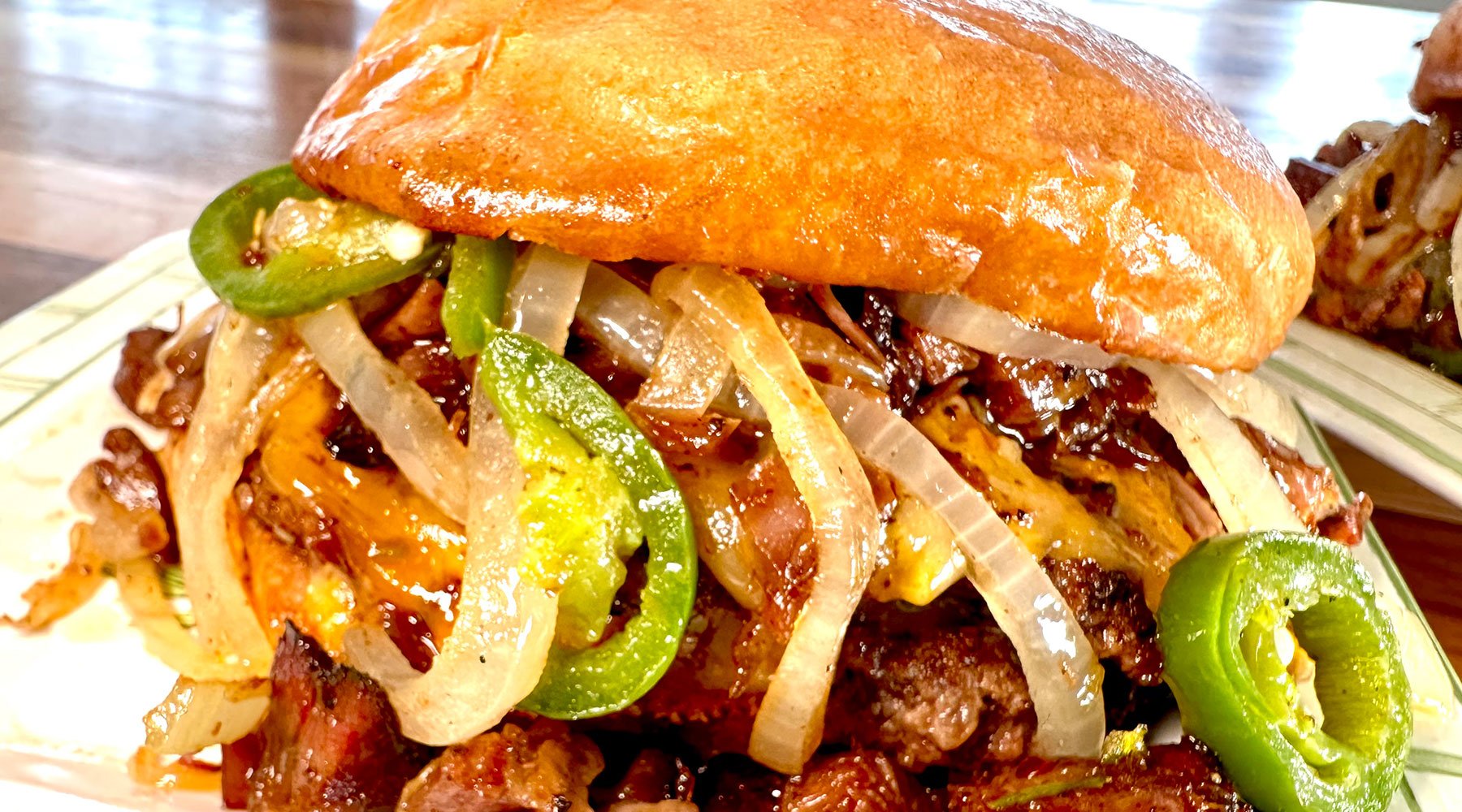 Ultimate BBQ sandwich that is stacked with smash burgers, burnt ends and topped with onions and jalapenos all dripping in Blues Hog Original BBQ Sauce.