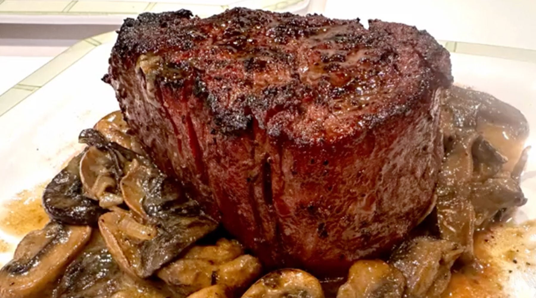 A thick, juicy grilled steak served on a bed of sautéed mushrooms in a savory sauce.