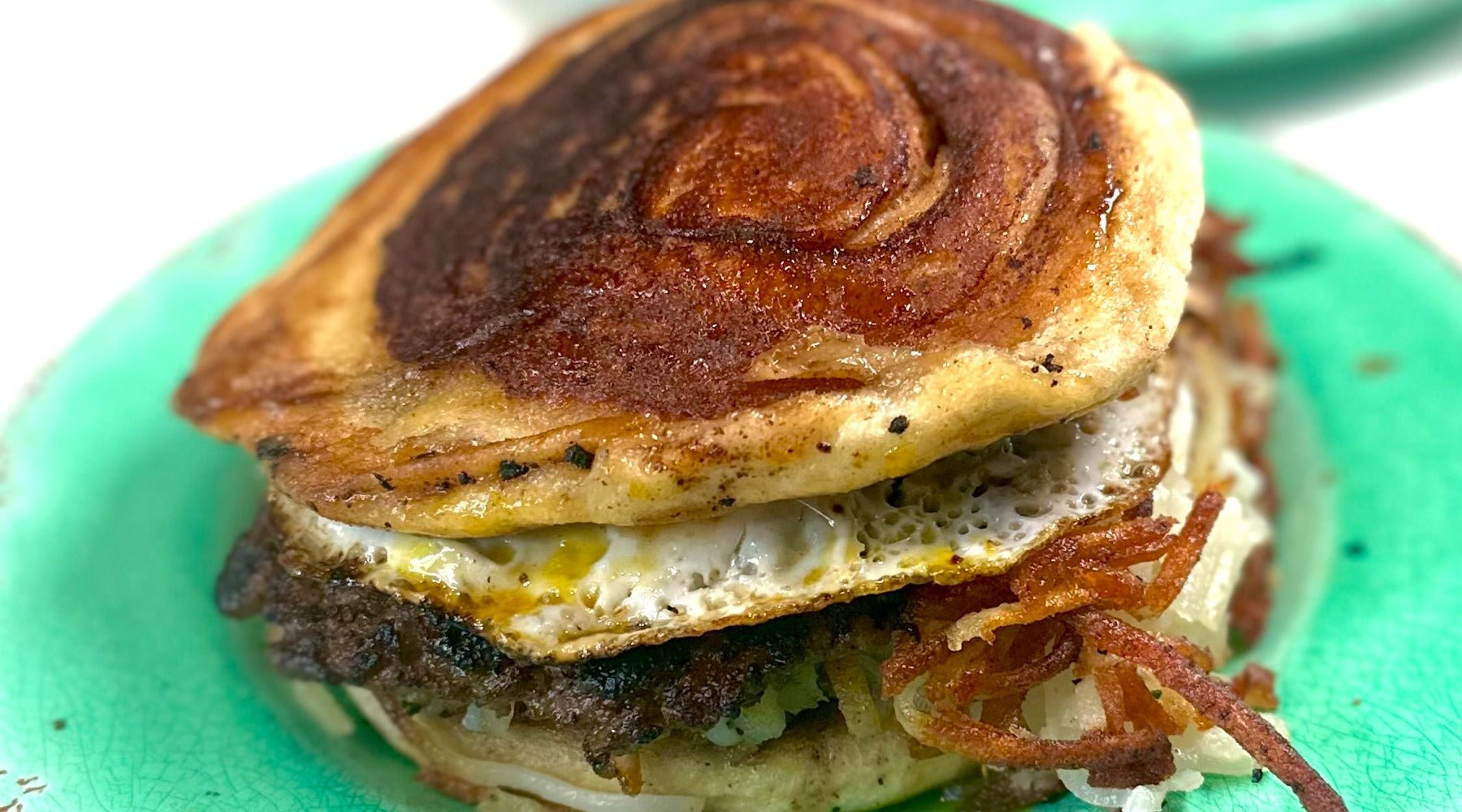 Cinnamon roll breakfast sandwich prepared on the griddle with sausage, hashbrowns and egg.