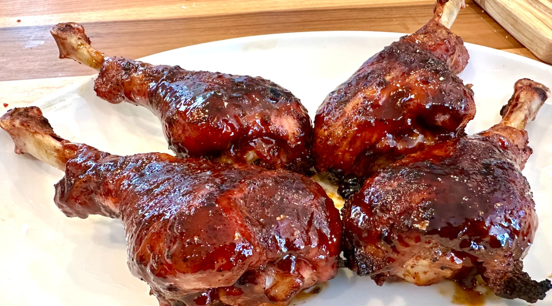 Four grilled turkey drumsticks covered in a glossy sauce, arranged on a white plate.