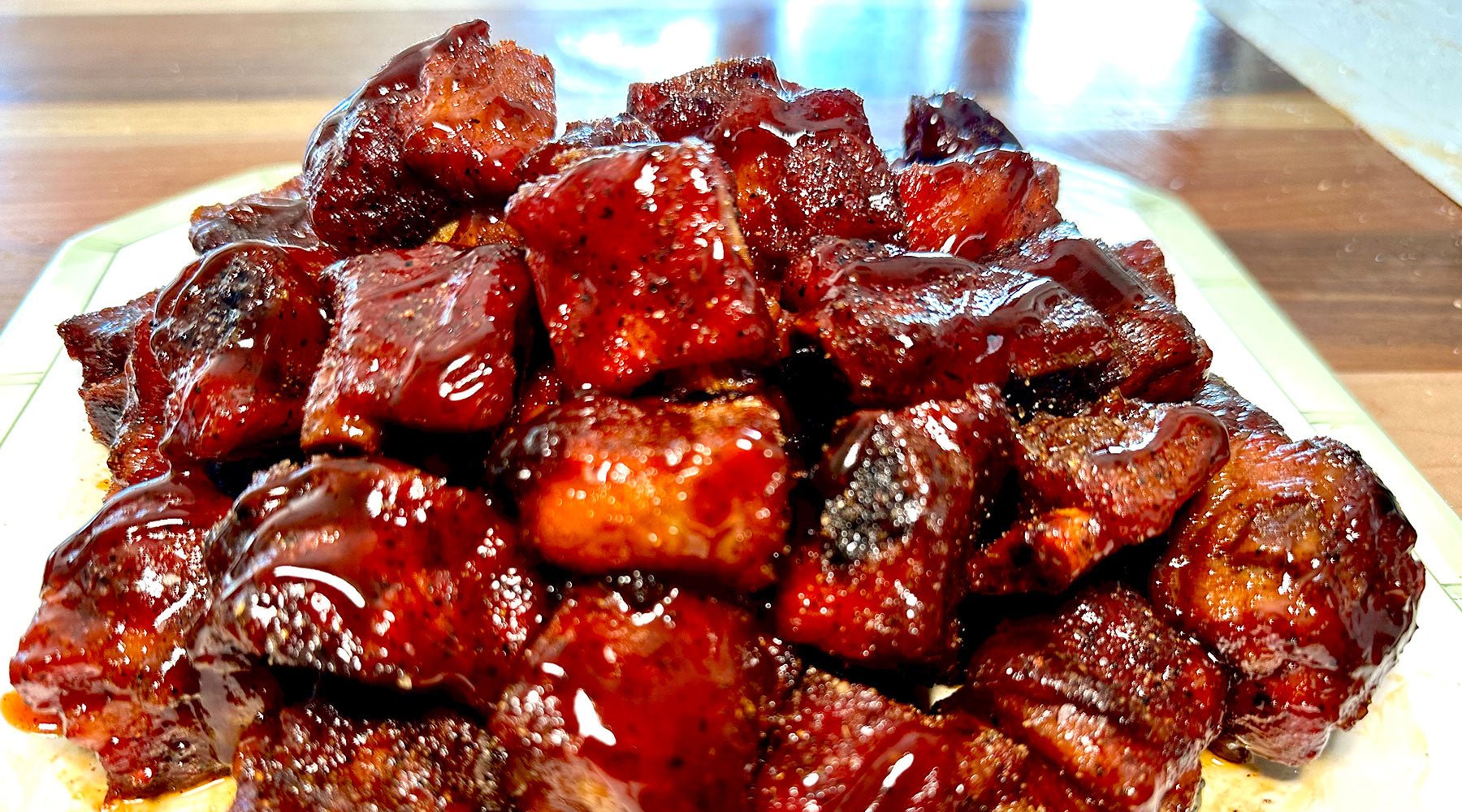 A pile of saucy, barbecued pork rib snacks arranged on a plate. The meat is covered in a shiny, dark red glaze, showcasing its tender and juicy texture with crispy edges.