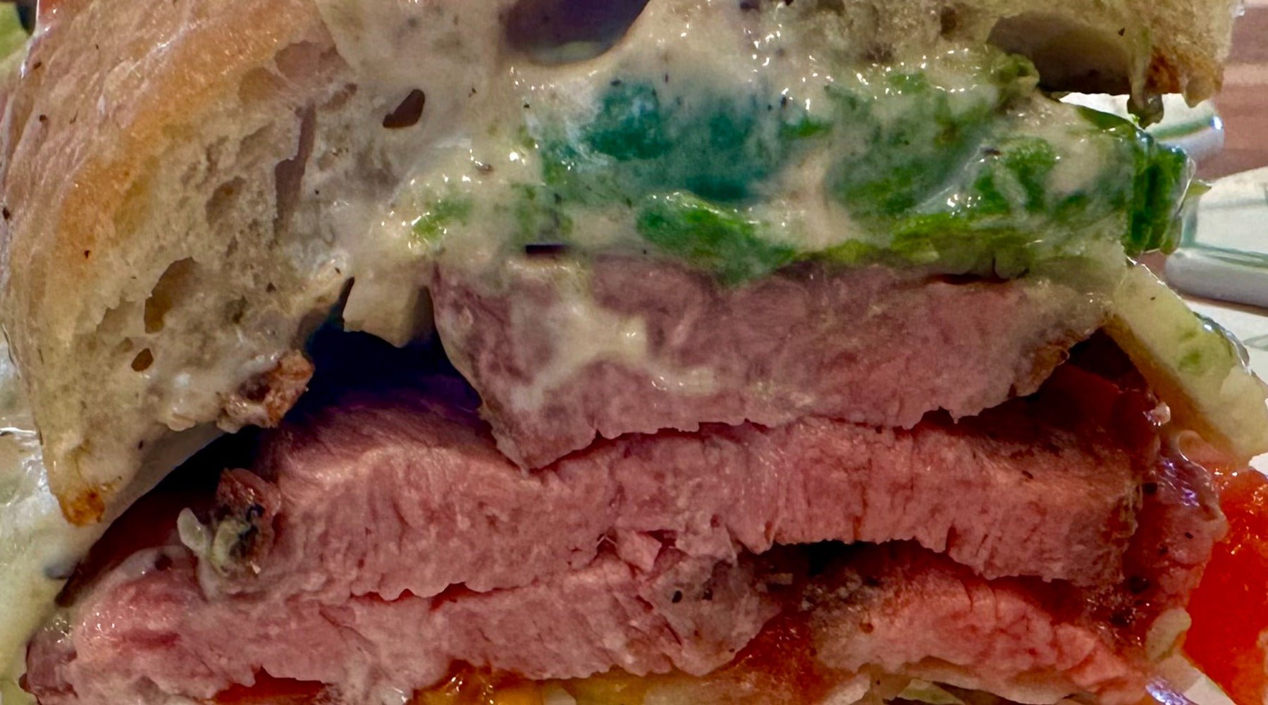 Upclose of a tri-tip sandwich on a ciabatti bread with horseradish dripping off it.