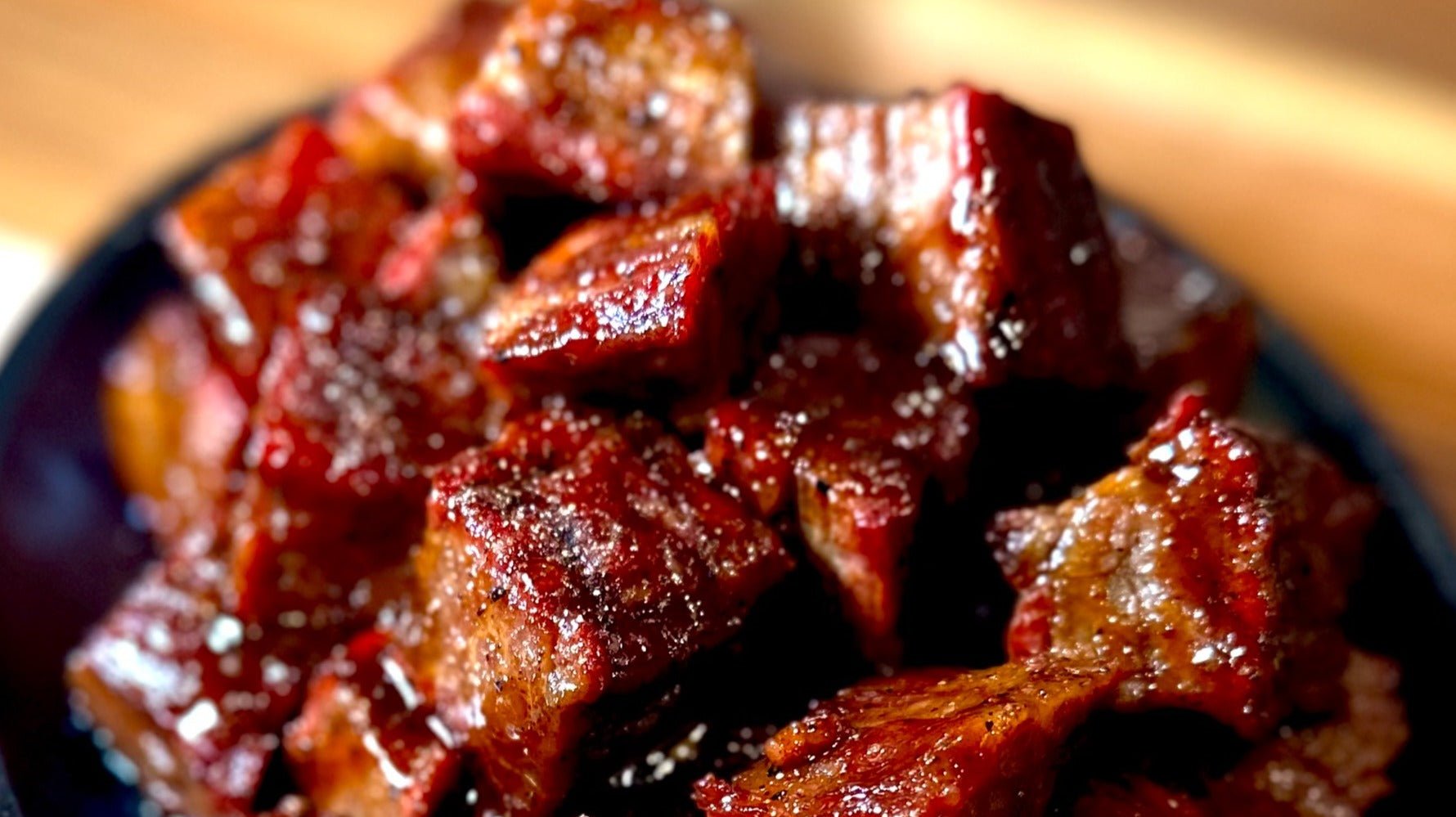 Upclose image of burnt ends in a cast iron dish on a cutting board.