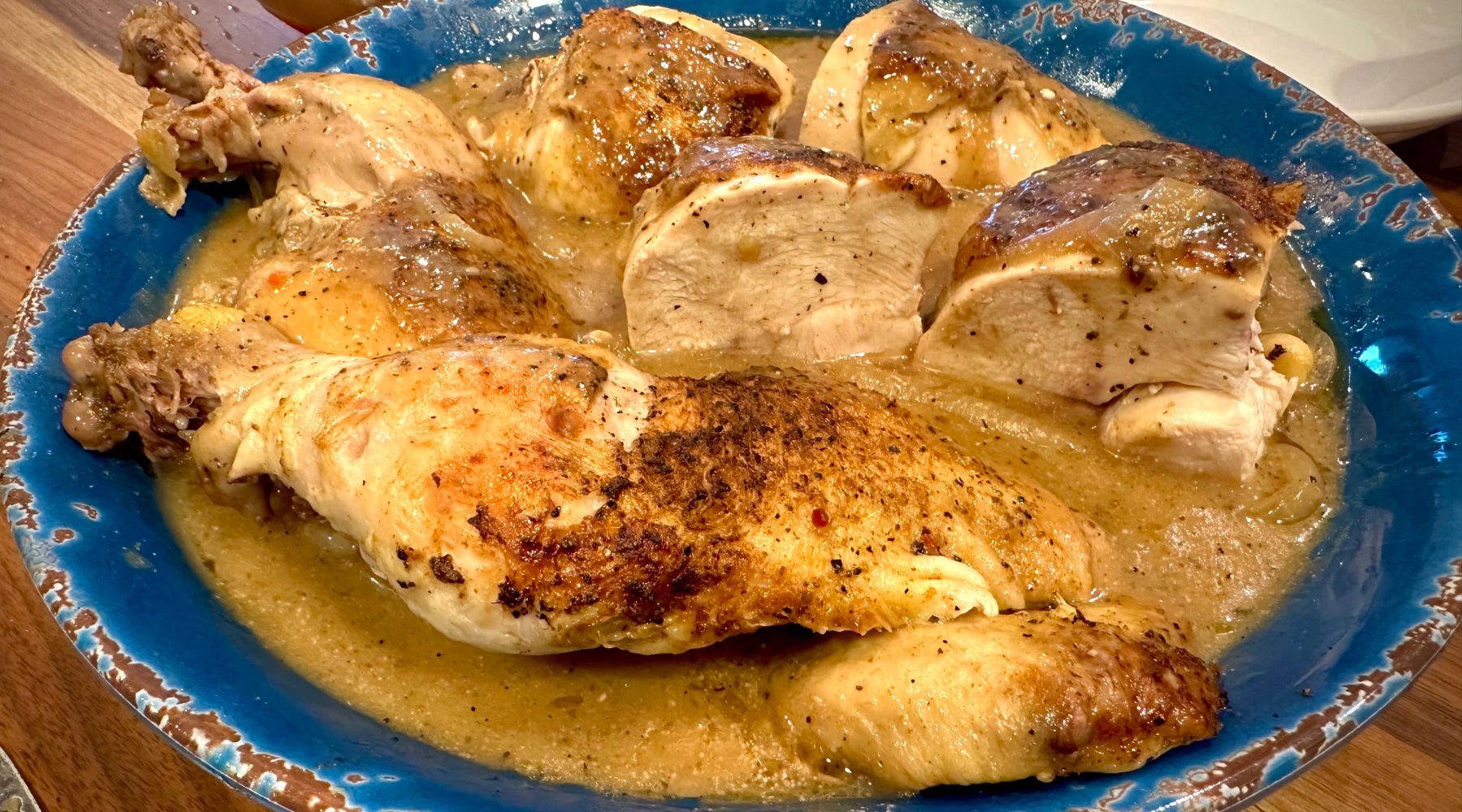 A blue plate filled with pieces of roasted chicken in a savory gravy.