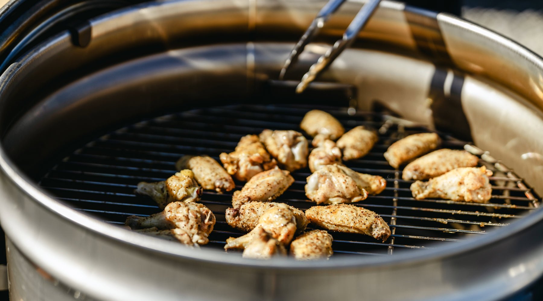 Up close of drum smoker that has chicken wings cooking.