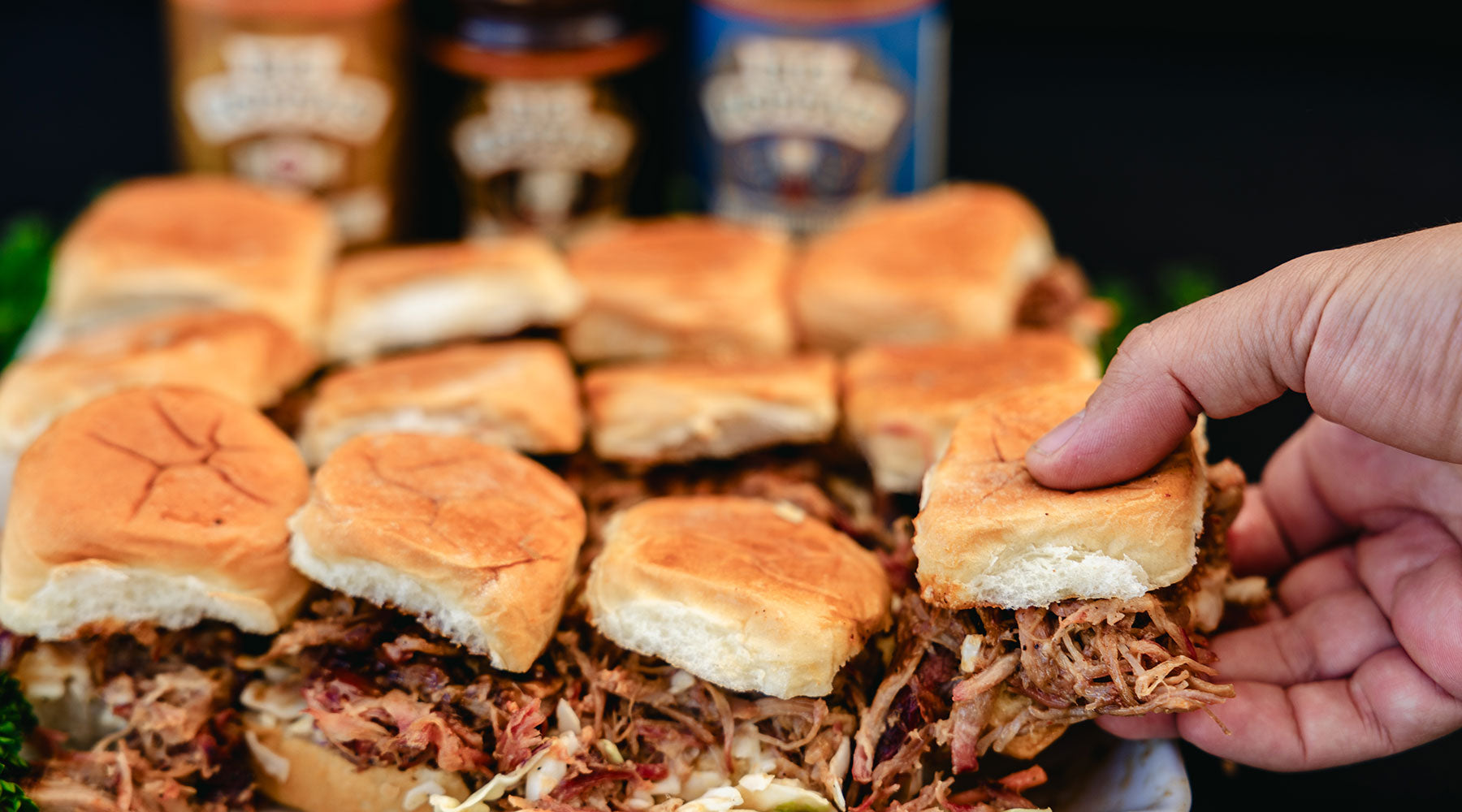 A hand reaching for a pulled pork slider on an King's Hawaiian roll.