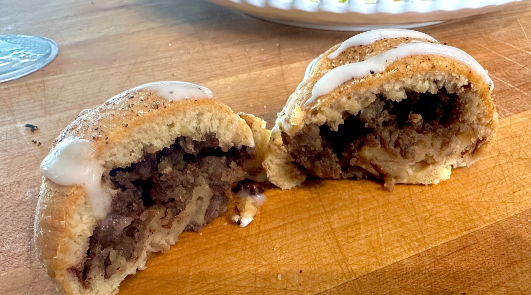 A sliced pastry filled with spiced ground meat and apples, topped with a drizzle of icing, displayed on a wooden surface.