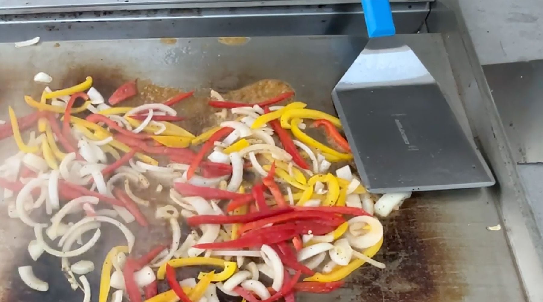 Vegetables and meat on the griddle cooking.