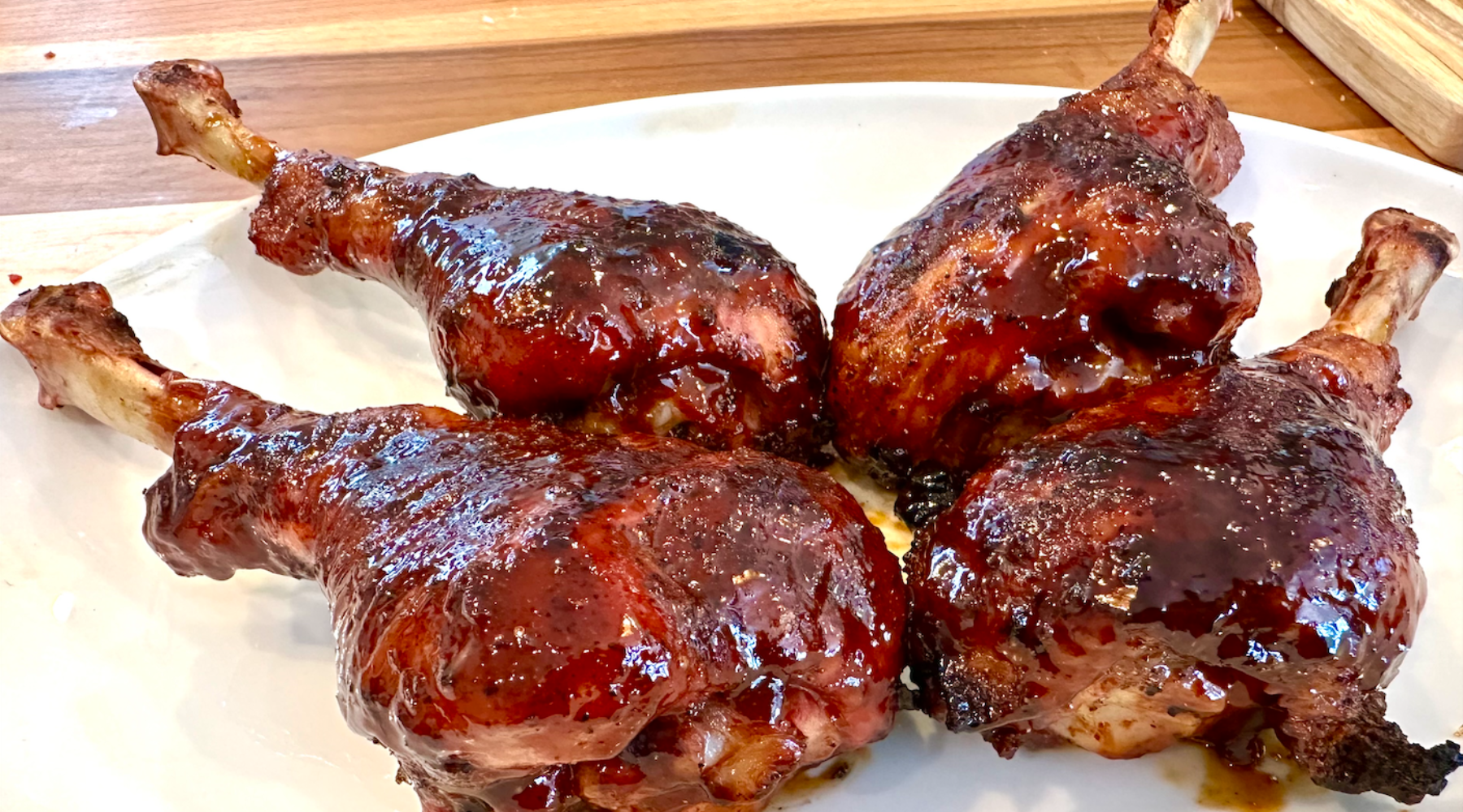 Four grilled turkey drumsticks covered in a glossy sauce, arranged on a white plate.